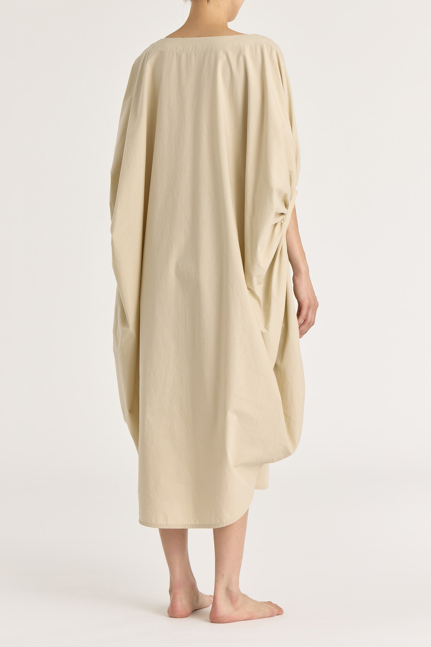 A model wearing a wide boat neck, voluminous sleeve, oyster-colored, loose-fitting cotton dress.