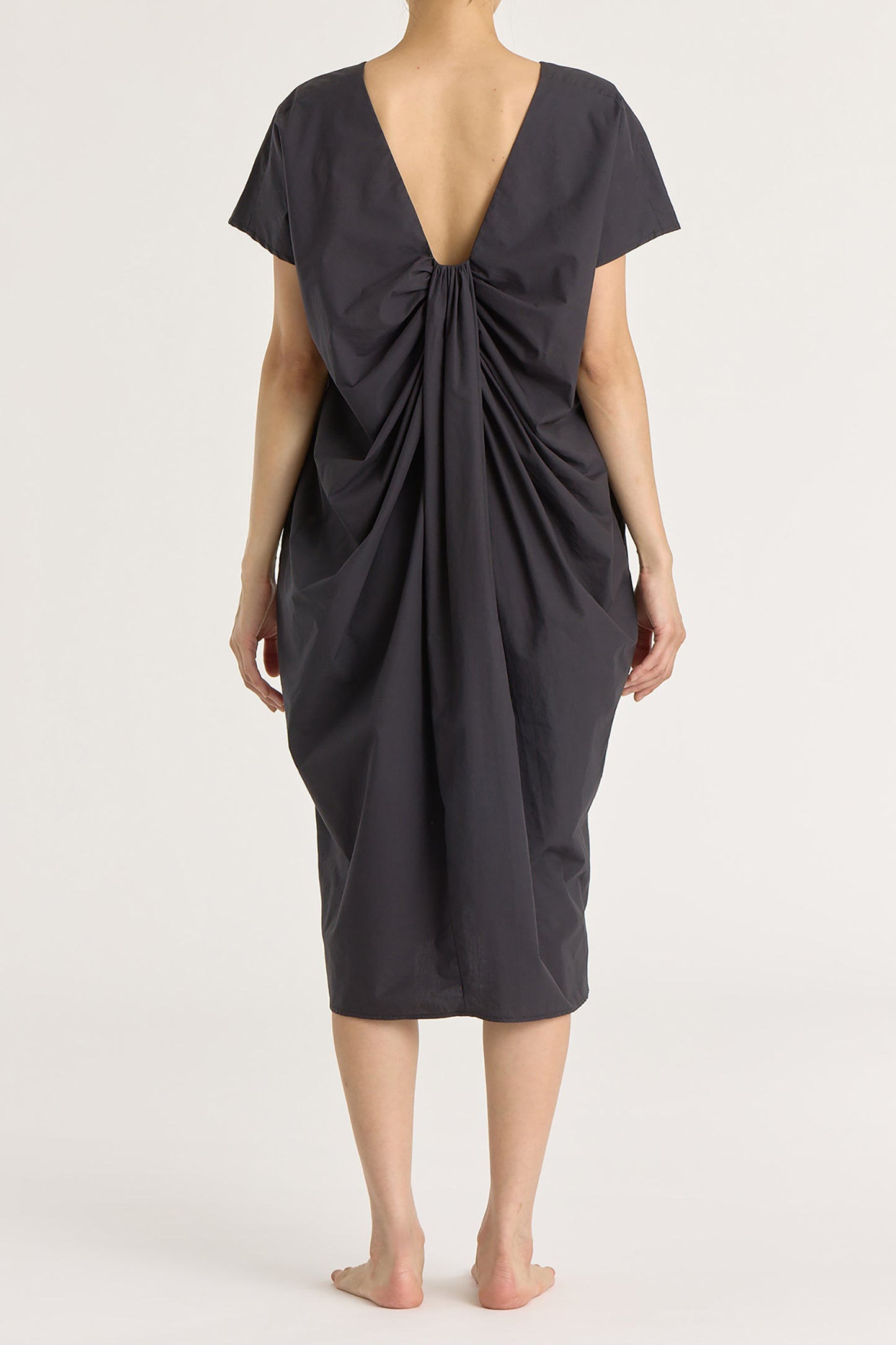 A model wearing a black crew neck dress with pleated details at the back and side seam pockets.