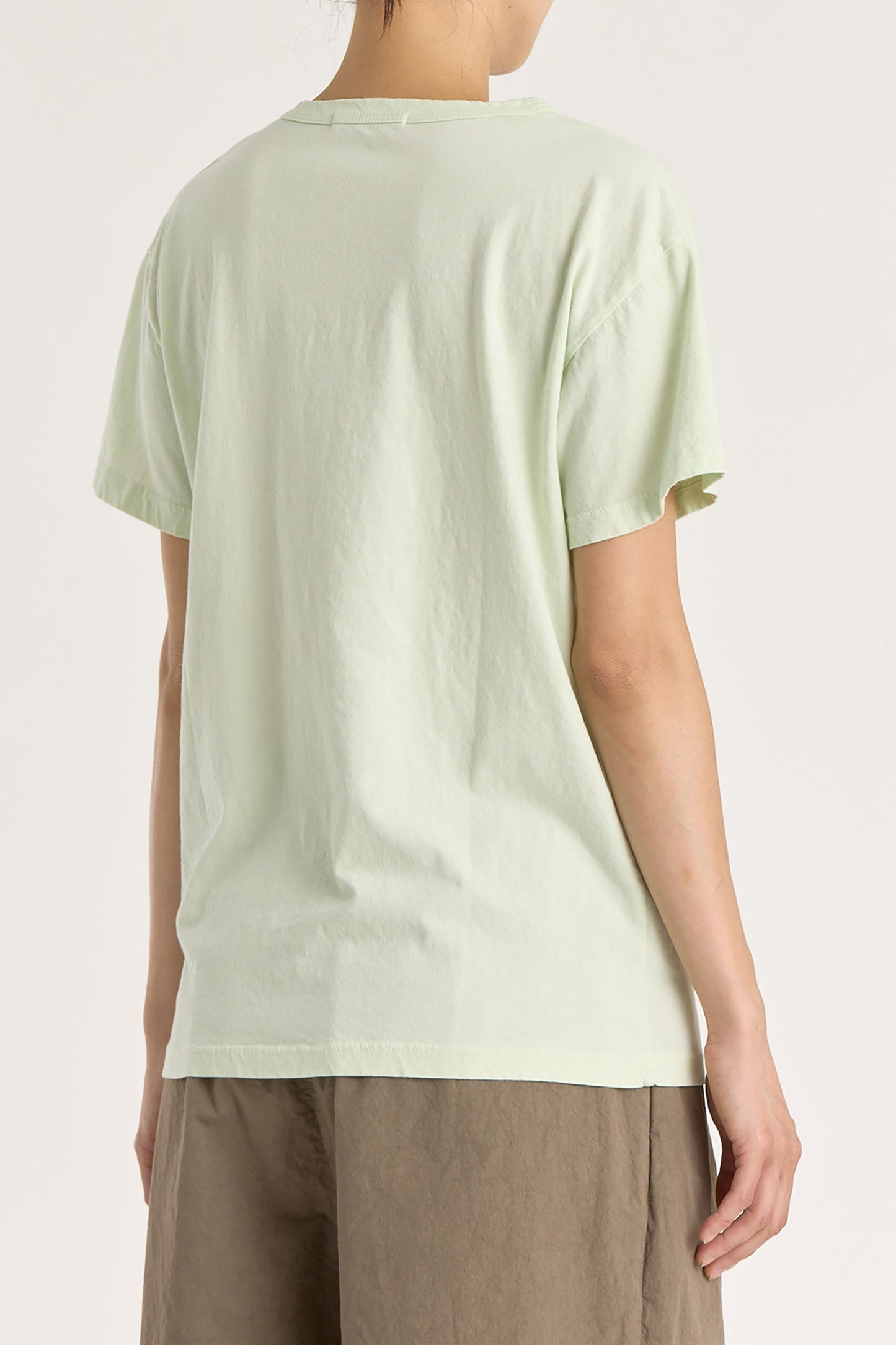 A person wearing a mint green basic crew neck t-shirt with short sleeves, paired with high-waisted trousers.