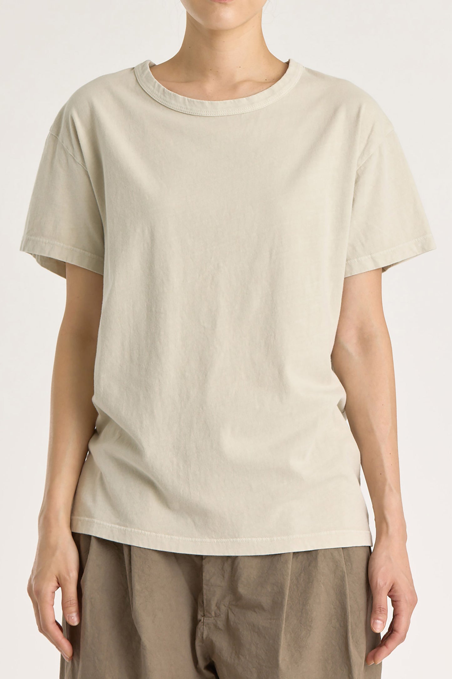 A person wearing a beige basic crew neck t-shirt with short sleeves, paired with high-waisted trousers.