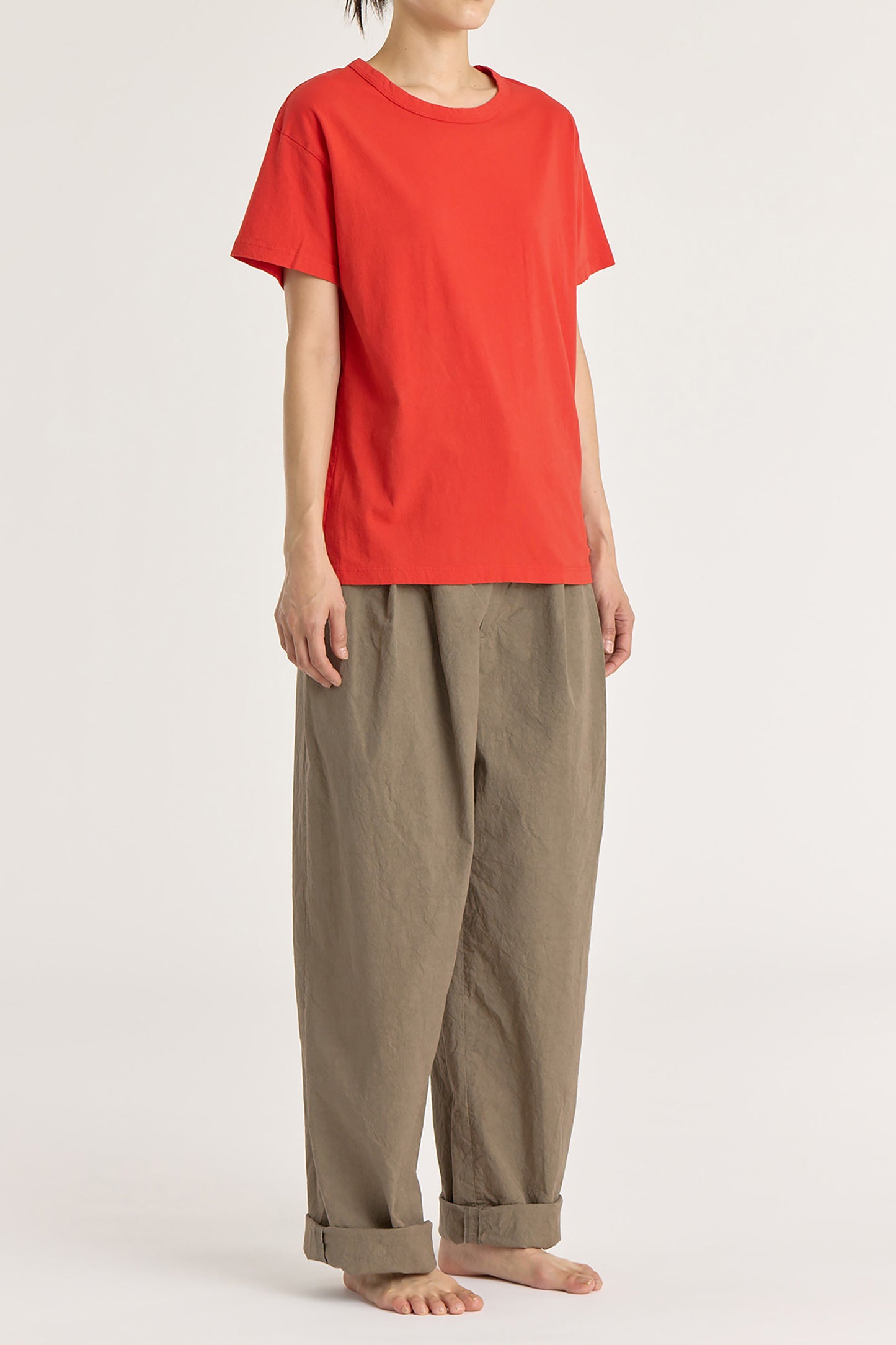 A person wearing a red basic crew neck t-shirt with short sleeves, paired with high-waisted trousers.