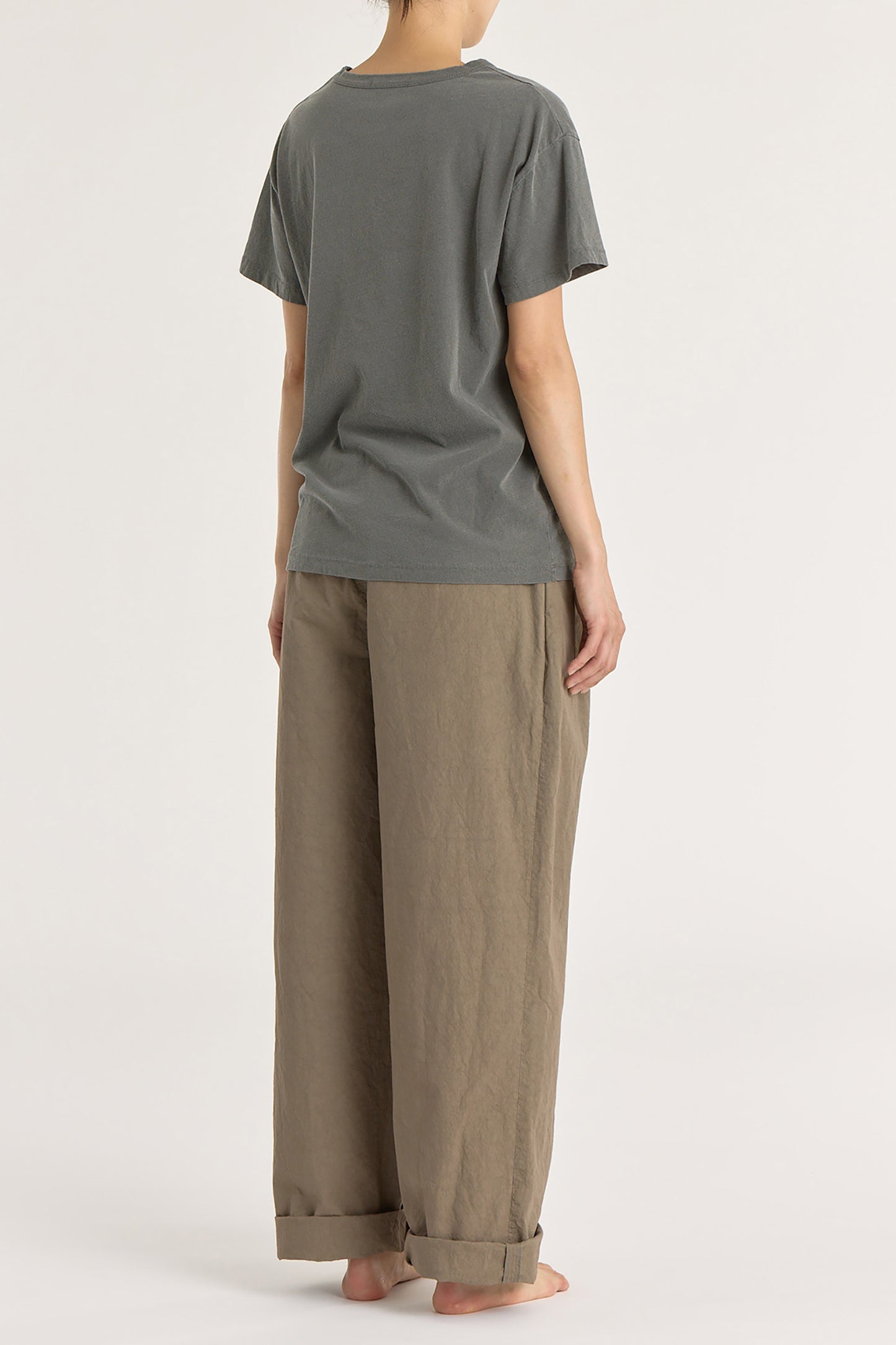 A person wearing a slate gray basic crew neck t-shirt with short sleeves, paired with high-waisted trousers.