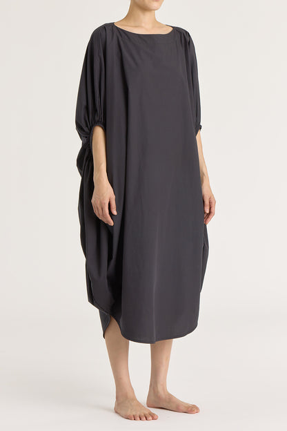 A person wearing a black teardrop dress with a wide boat neck and voluminous sleeves, loose-fitting cotton dress.