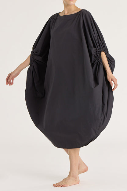 A person wearing a black teardrop dress with a wide boat neck and voluminous sleeves, loose-fitting cotton dress.