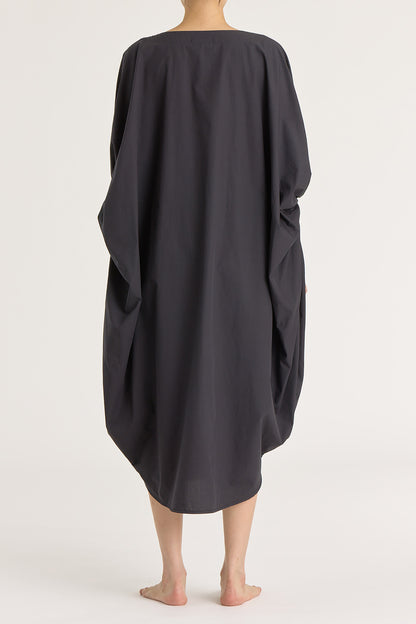 A person wearing a black teardrop dress with a wide boat neck and voluminous sleeves, loose-fitting cotton dress.