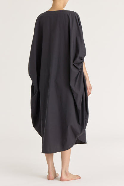 A person wearing a black teardrop dress with a wide boat neck and voluminous sleeves, loose-fitting cotton dress.
