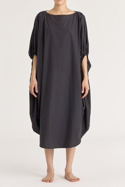 A person wearing a black teardrop dress with a wide boat neck and voluminous sleeves, loose-fitting cotton dress.