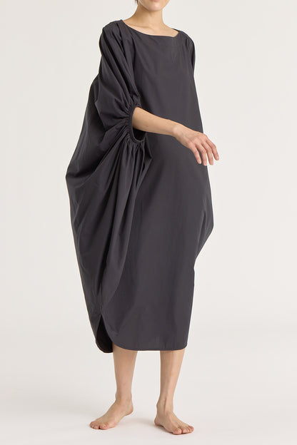 A person wearing a black teardrop dress with a wide boat neck and voluminous sleeves, loose-fitting cotton dress.