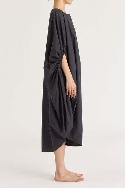 A person wearing a black teardrop dress with a wide boat neck and voluminous sleeves, loose-fitting cotton dress.