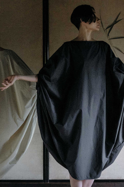 A person wearing a black, voluminous sleeve dress with a wide boat neckline. The dress is made of soft cotton fabric.