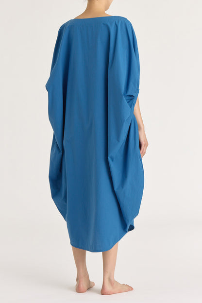 A person wearing a blue teardrop dress with a wide boat neck and voluminous sleeves, loose-fitting cotton dress.