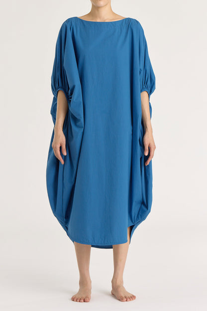 A person wearing a blue teardrop dress with a wide boat neck and voluminous sleeves, loose-fitting cotton dress.