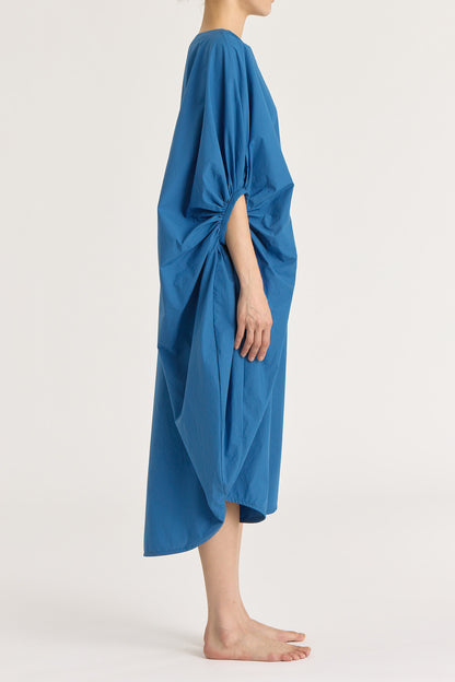 A person wearing a blue teardrop dress with a wide boat neck and voluminous sleeves, loose-fitting cotton dress.