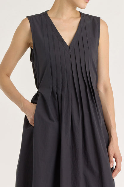 A model wearing a black pleated V-neck dress with side seam pockets and an adjustable drawstring at the back.