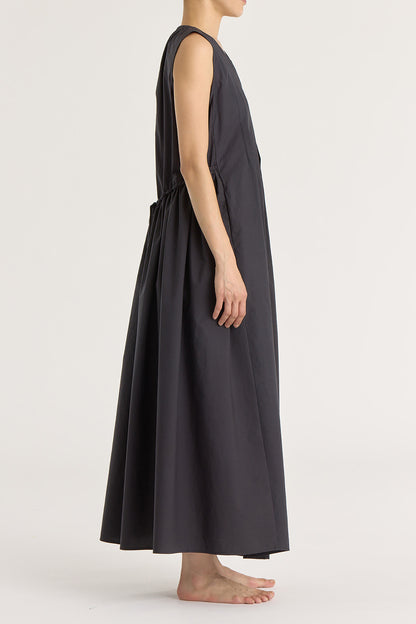 A model wearing a black pleated V-neck dress with side seam pockets and an adjustable drawstring at the back.