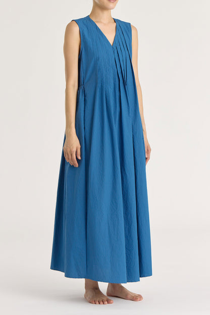 A model wearing a blue pleated V-neck dress with side seam pockets and an adjustable drawstring at the back.