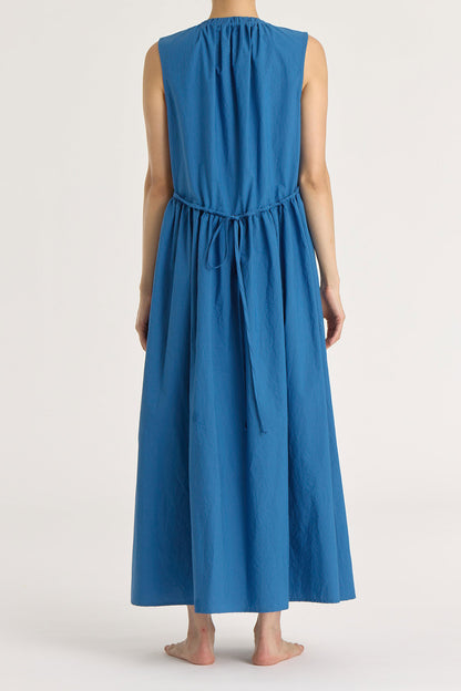 A model wearing a blue pleated V-neck dress with side seam pockets and an adjustable drawstring at the back.