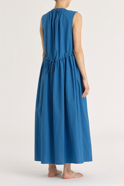 A model wearing a blue pleated V-neck dress with side seam pockets and an adjustable drawstring at the back.