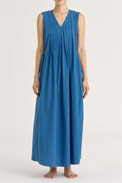 A model wearing a blue pleated V-neck dress with side seam pockets and an adjustable drawstring at the back.