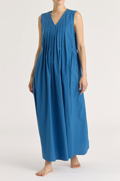 A model wearing a blue, pleated V-neck sleeveless maxi dress with side seam pockets.
