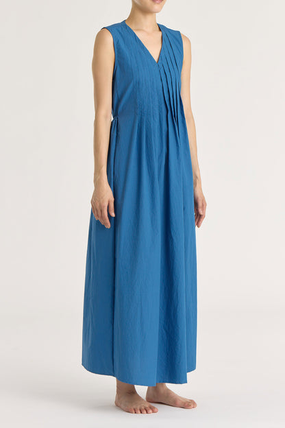A model wearing a blue pleated V-neck dress with side seam pockets and an adjustable drawstring at the back.