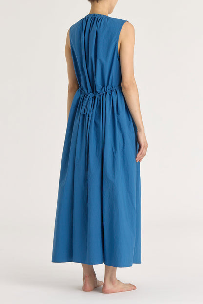 A model wearing a blue pleated V-neck dress with side seam pockets and an adjustable drawstring at the back.