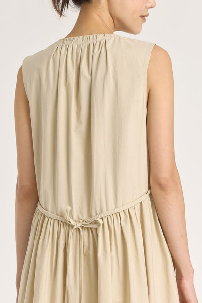 A model wearing a beige pleated V-neck dress with side seam pockets and an adjustable drawstring at the back.