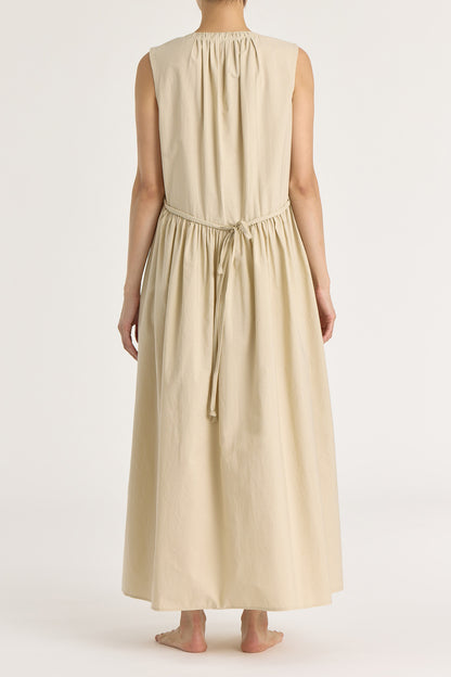 A model wearing a beige pleated V-neck dress with side seam pockets and an adjustable drawstring at the back.