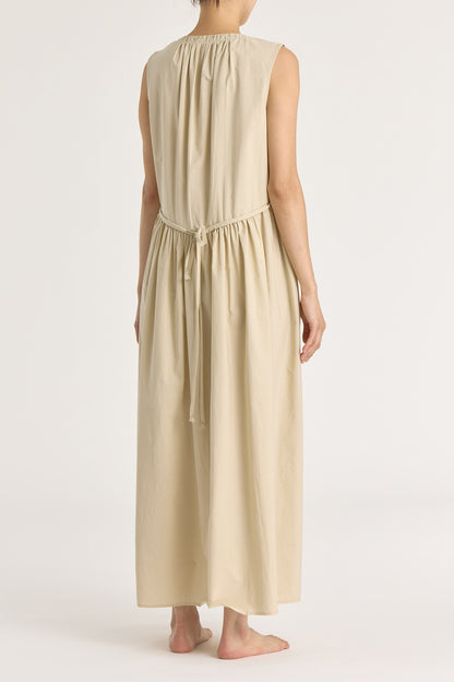 A model wearing a beige pleated V-neck dress with side seam pockets and an adjustable drawstring at the back.
