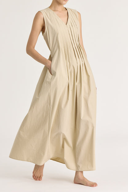 A model wearing a beige pleated V-neck dress with side seam pockets and an adjustable drawstring at the back.