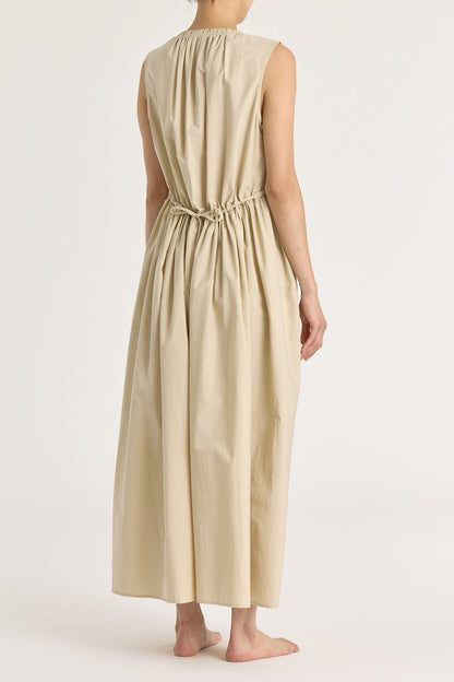 A model wearing a beige pleated V-neck dress with side seam pockets and an adjustable drawstring at the back.