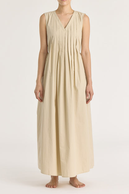 A model wearing a beige pleated V-neck dress with side seam pockets and an adjustable drawstring at the back.
